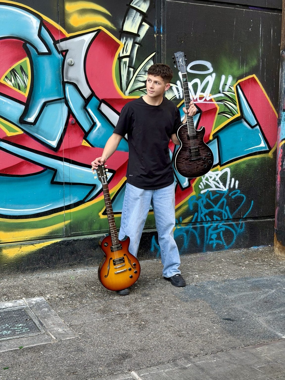 Donnie with two guitars in front of graffiti